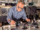 NIST physicist Dave Howe aligns a laser beam to pass through a tiny glass cell of rubidium atoms inside the cylindrical magnetic shield. The atoms are the heart of an atomic magnetometer demonstrated as a receiver for digitally modulated magnetic VLF signals. NIST scientists hope further advances in receivers and transmitters could improve communication and mapping indoors at long range, in urban canyons, underwater, and underground. [NIST photo]